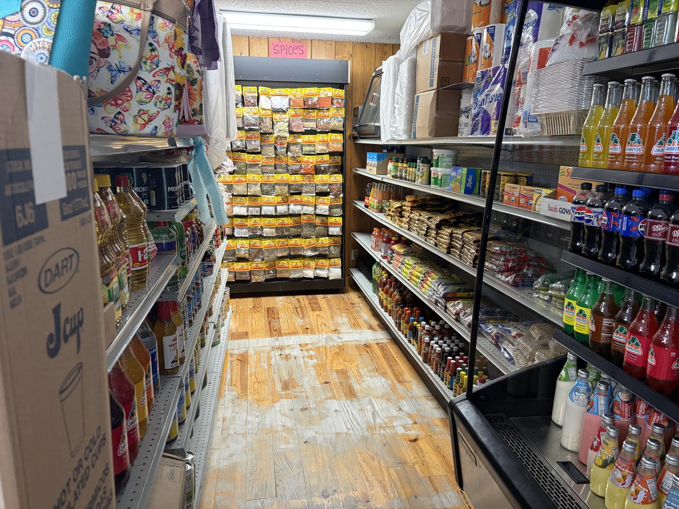 A market aisle with spices, hot sauces, dried goods and bottled drinks