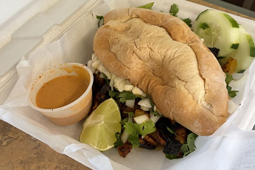A torta on a toasted roll with cilantro, onion, lime and a cup of hot sauce